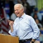 Man speaking at podium with crowd background.