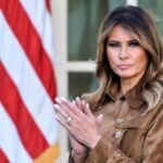 Woman standing near American flag, clapping her hands.