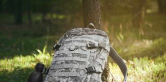 Camouflage backpack and canteen beside a tree.