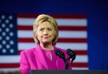 Person in pink suit speaking with American flag backdrop.