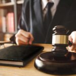 Judge holding gavel near glasses and notebook