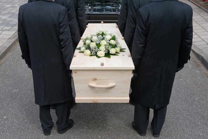 144558722 featured image Four people carrying a coffin with white flowers.