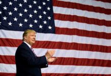 Man clapping in front of large American flag