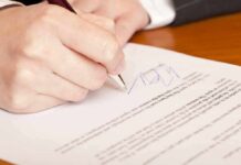 Hand signing a document on a wooden table