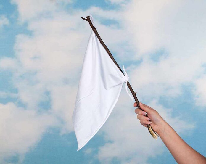 84861409 featured image Hand holding white flag against a blue sky.