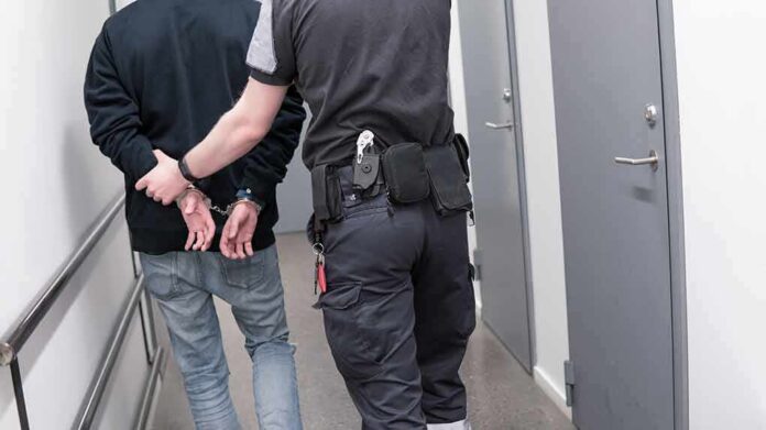 Officer escorting handcuffed person down hallway