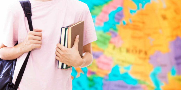 1180054603 featured image Person holding books in front of a colorful map