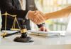 Hands shaking over legal documents with gavel and scales