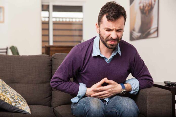 344063903 featured image Man sitting on couch, holding stomach in pain