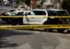 Police tape blocking street with patrol cars