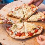 People sharing slices of pizza on a wooden board