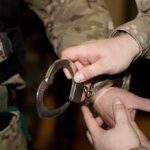 A military personnel placing handcuffs on an individual