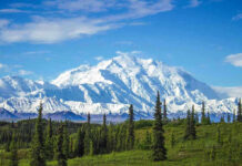 Snow-covered mountain under blue sky with green foreground