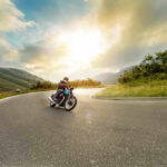 Person rides motorcycle on curved mountain road at sunset