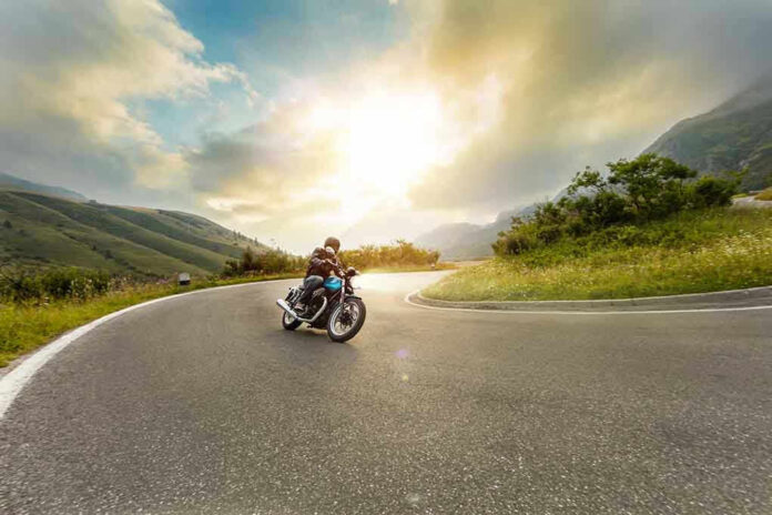 Person rides motorcycle on curved mountain road at sunset