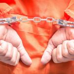 Fatal Firearm Stunt – Unbelievable! Hands in handcuffs wearing an orange jumpsuit