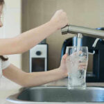 Girl filling glass with water from kitchen faucet.