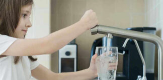 Girl filling glass with water from kitchen faucet.