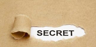 A torn piece of brown paper revealing the word SECRET underneath