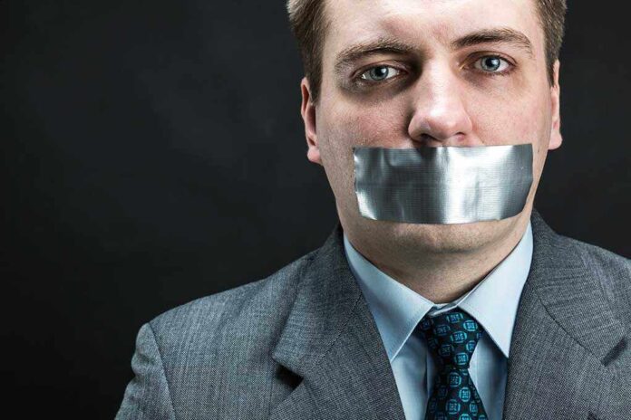 Man in business attire with duct tape over his mouth, conveying a message about silence