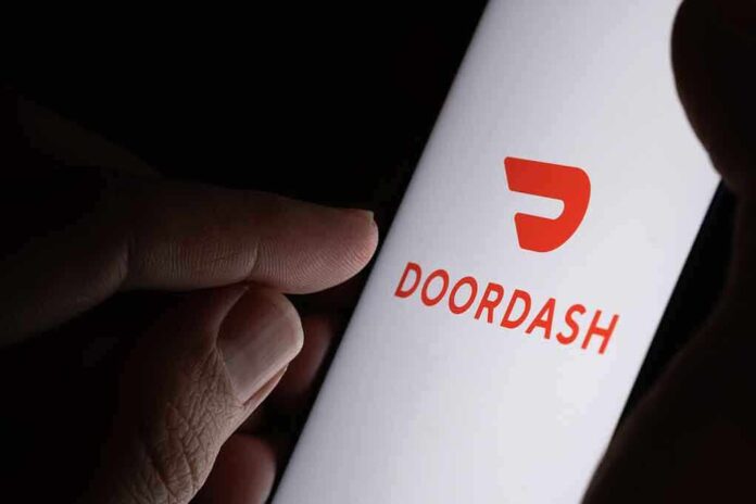 A hand holding a smartphone displaying the Doordash logo