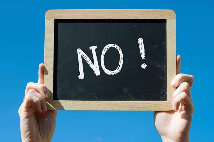 A hand holding a chalkboard with the word NO! written on it against a blue sky