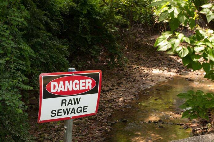 Warning sign indicating danger due to raw sewage near a creek