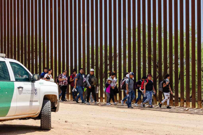 People walking beside tall fence and border patrol vehicle.