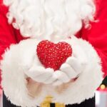 Santa Claus holding a red heart in front of a festive background