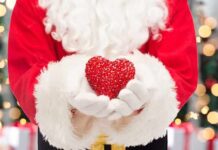 Santa Claus holding a red heart in front of a festive background