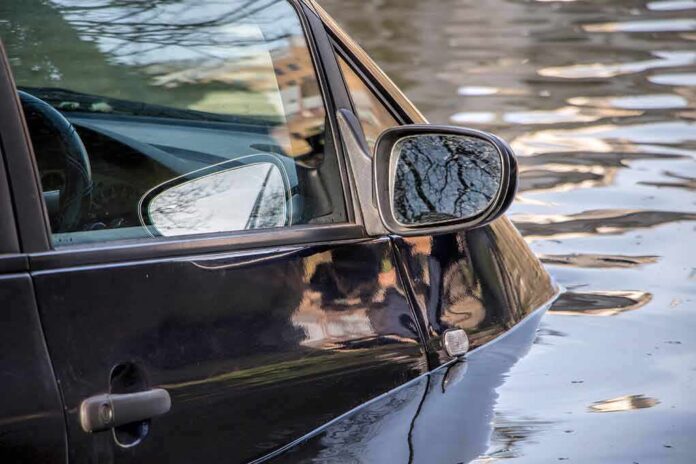 A partially submerged black car in floodwaters