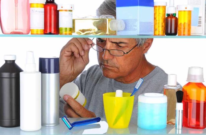 Senior man looking closely at a product in a medicine cabinet filled with various bottles and containers