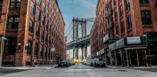 Street view with bridge between two brick buildings.