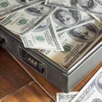 Breaking: Police Chief’s Massive Embezzlement EXPOSED! A briefcase filled with hundred dollar bills on a wooden surface