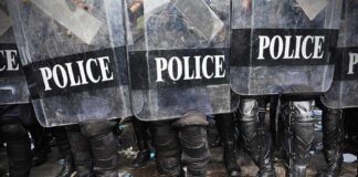 Police officers in riot gear standing behind shields marked POLICE