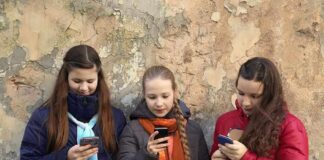 Three teenagers using smartphones while standing against a textured wall