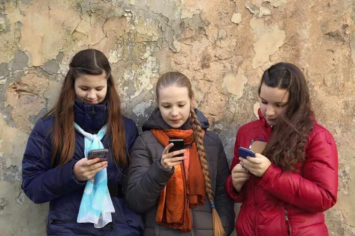 Three teenagers using smartphones while standing against a textured wall