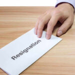 Hand holding a resignation letter on table.
