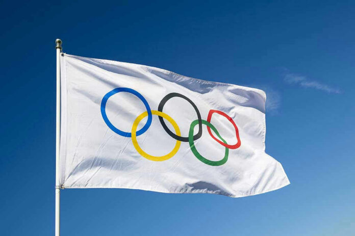 Olympic flag waving against clear blue sky.