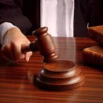 A judges hand holding a gavel over a wooden desk with law books