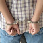 Disturbing Allegations: Obscenity, Dogs, and Minors A person in handcuffs viewed from behind, wearing a plaid shirt and denim jeans