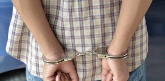 A person in handcuffs viewed from behind, wearing a plaid shirt and denim jeans