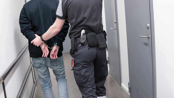 Officer escorting handcuffed person down hallway.