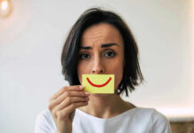 Woman holding smiley face card over mouth