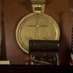 DOJ and Google Slammed in Epstein Victim Leak A judges bench in a courtroom with a gavel and flags