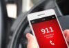 A smartphone displaying the emergency number 911 while held in a persons hand inside a car