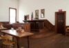 Interior of a historic courtroom with wooden furniture and an American flag