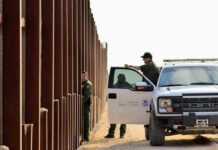 Candidate’s Bold Move: Arrest ICE Officers! Border patrol agents near a tall metal fence.