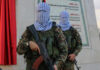 Masked soldiers holding rifles in front of a monument.