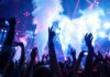 Crowd at a concert with hands raised and smoke effects in the background
